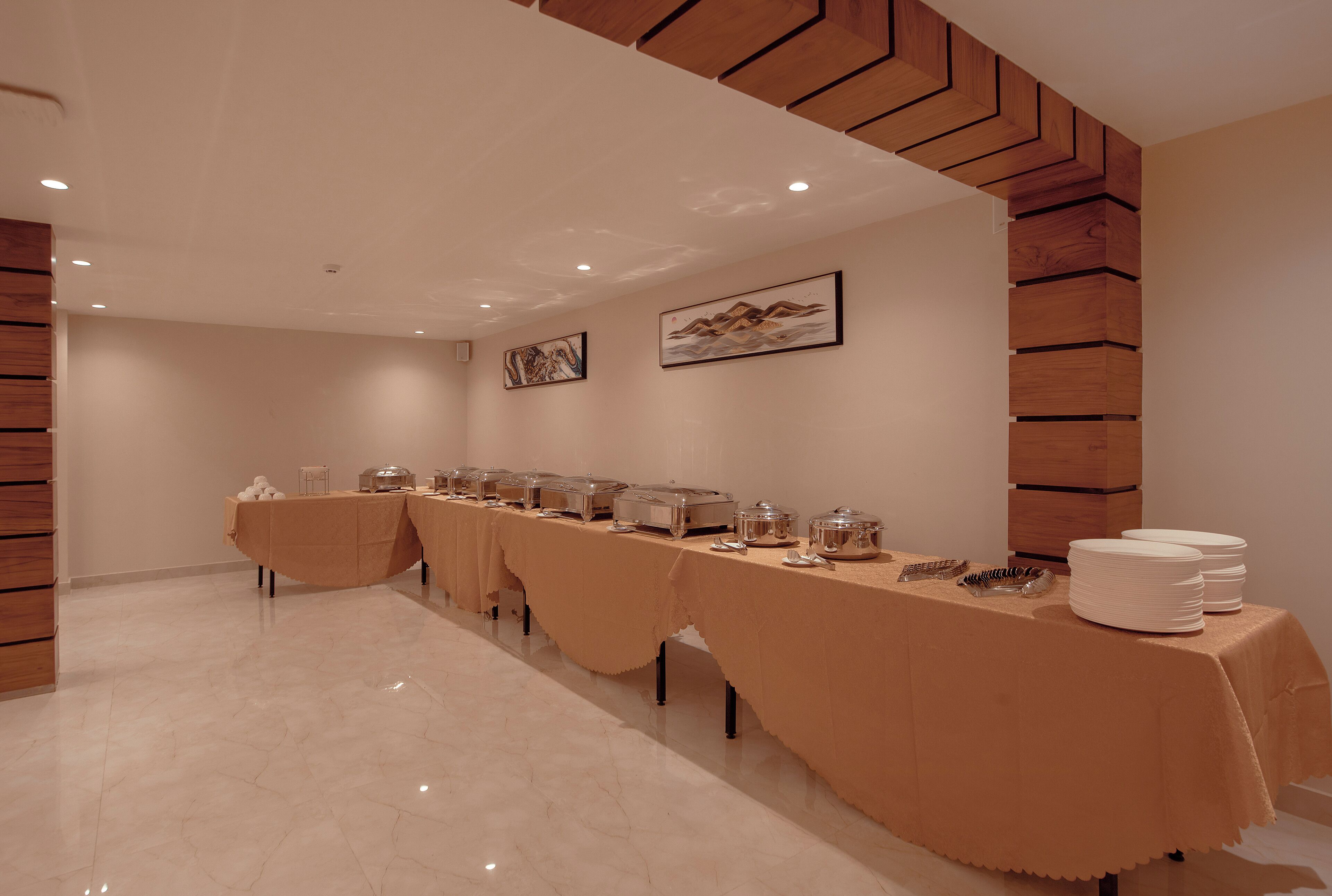 Una larga mesa con recipientes de comida, platos y una pila de platos blancos a la derecha.