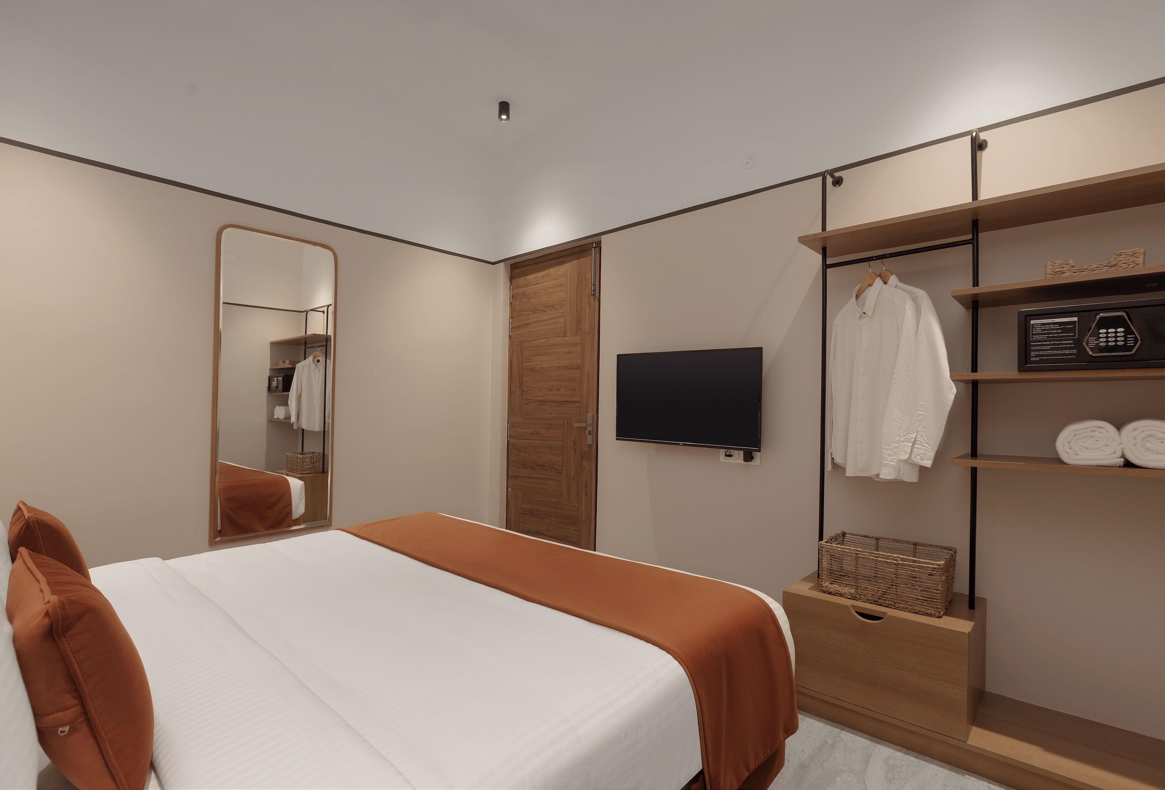 Quarto de hotel moderno com uma cama grande, televisão, guarda-roupa com prateleiras e espelho.