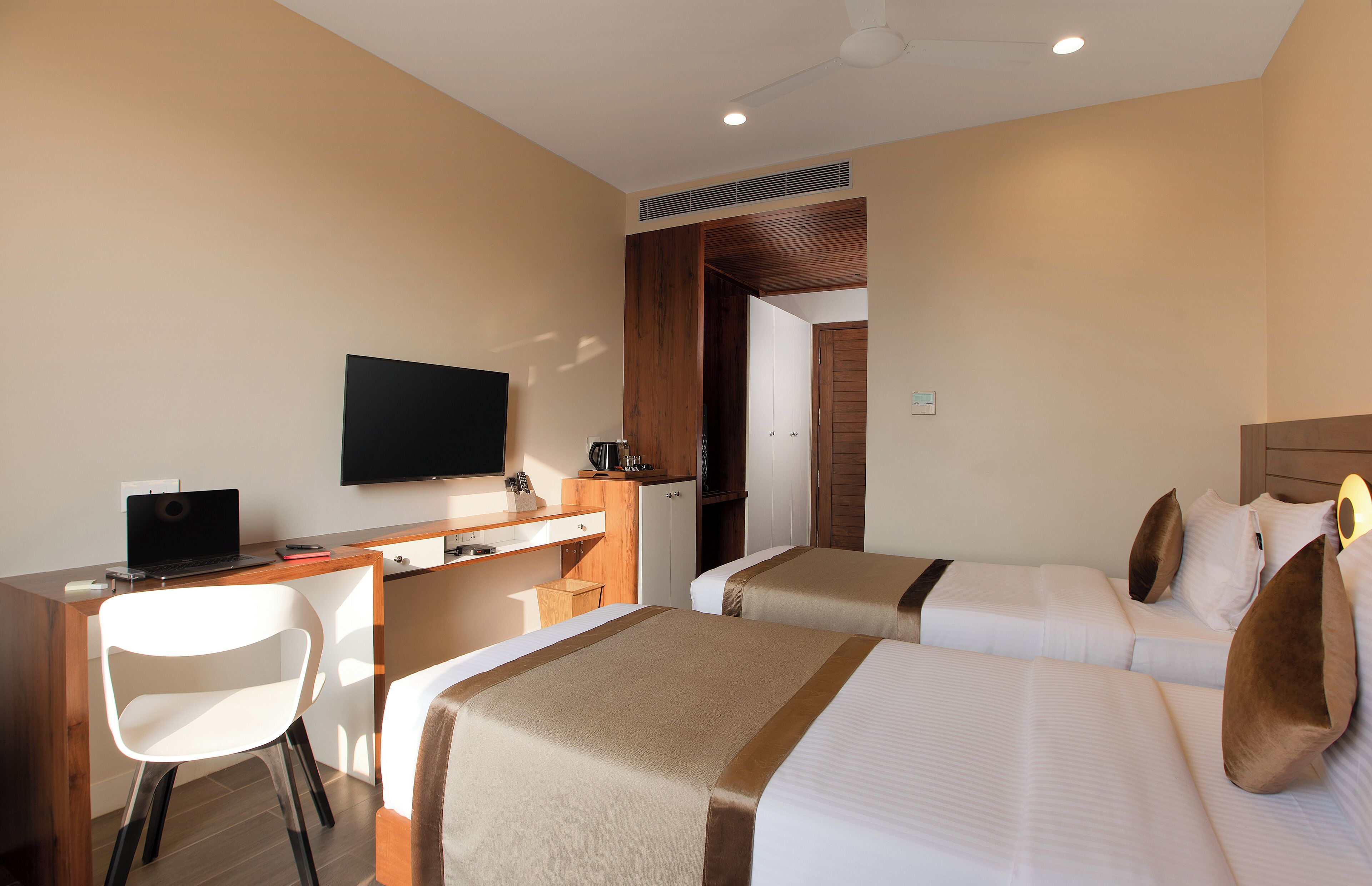 Quarto de hotel com escrivaninha, duas camas, televisão e guarda-roupa.