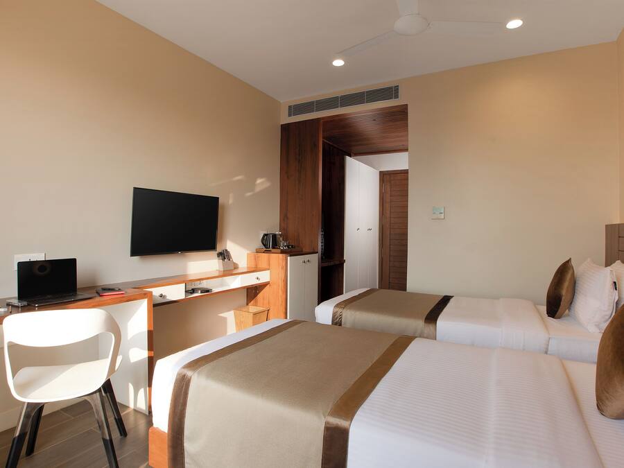 Quarto de hotel com escrivaninha, duas camas, televisão e guarda-roupa.