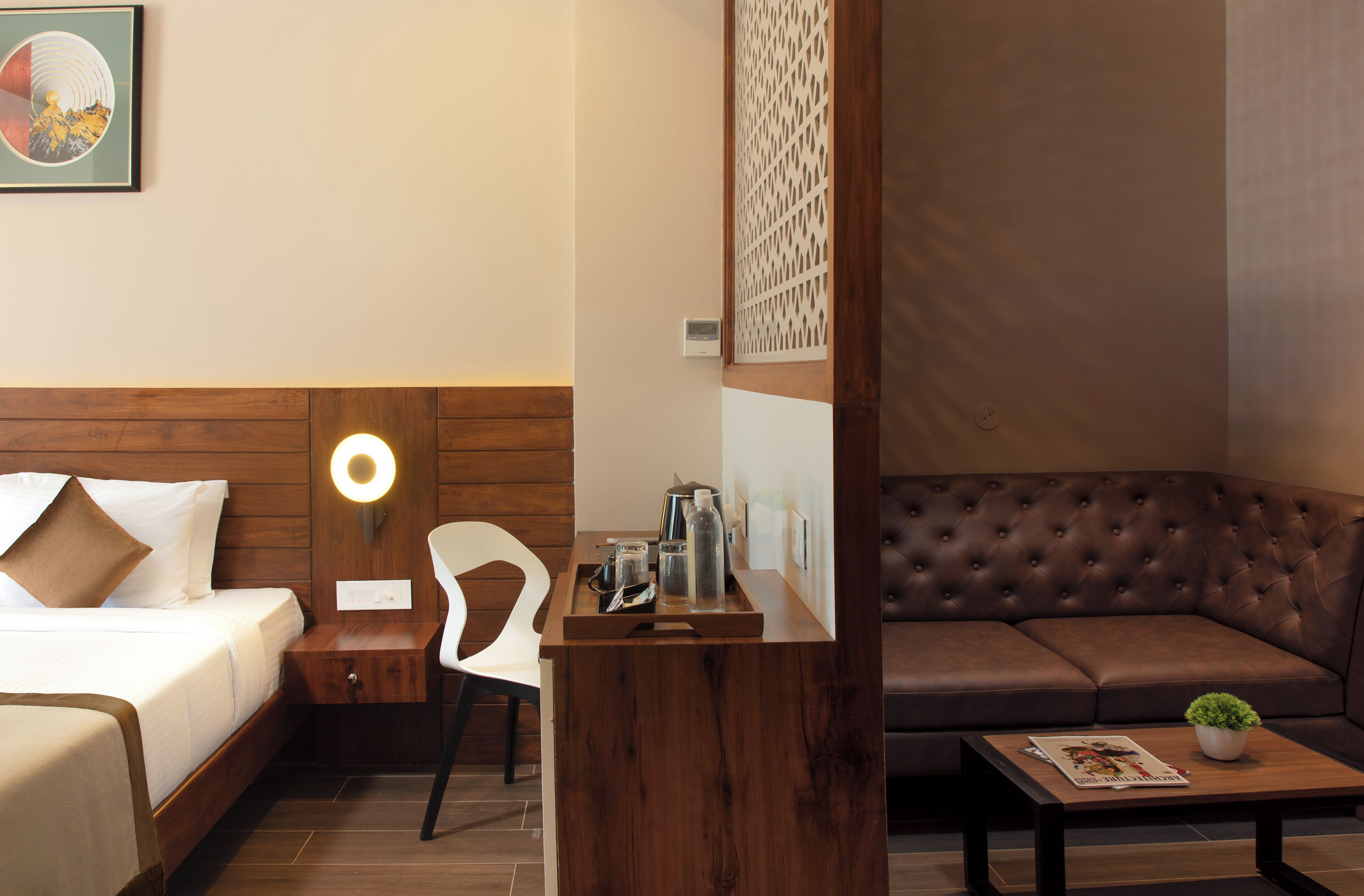 Une chambre d’hôtel comprenant un lit, une table de chevet, une chaise, un buffet en bois et un canapé en cuir marron.