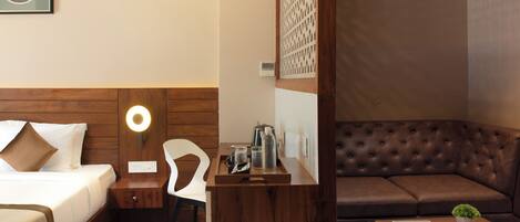 Habitación de hotel con cama, mesita de noche, silla, aparador de madera y sofá de cuero marrón.
