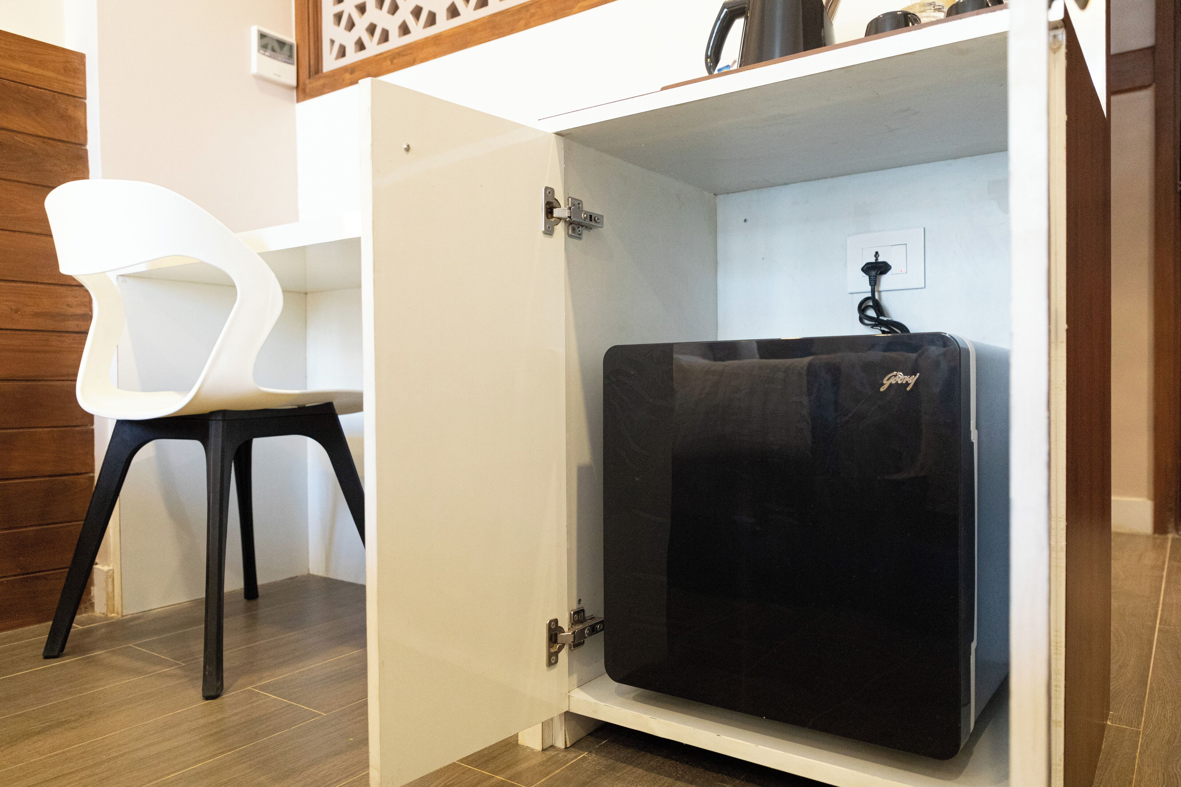 Una cocina compacta con un refrigerador negro, una silla blanca y un gabinete de madera.