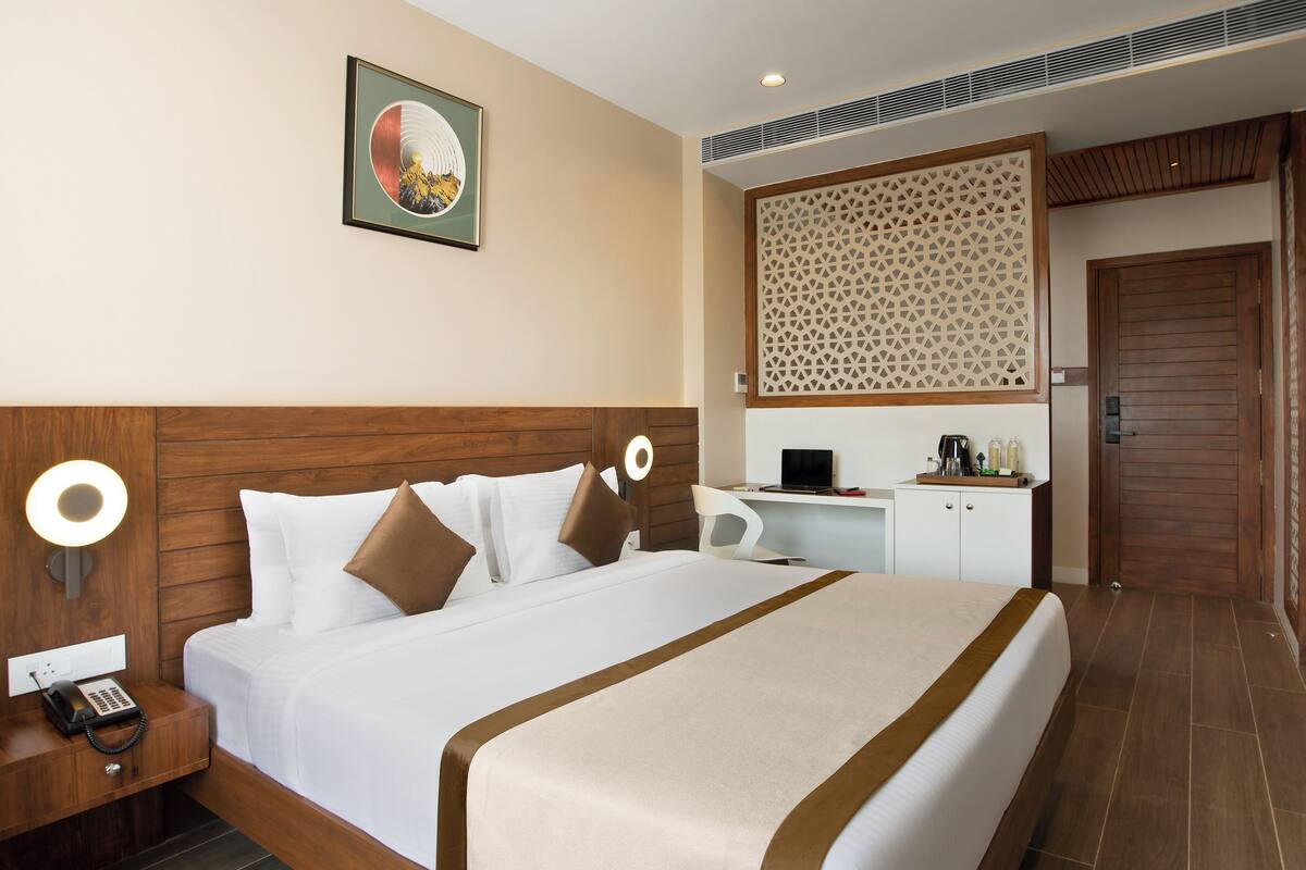 A hotel room with a large bed, a desk with a computer, a phone, and a decorative wall panel.