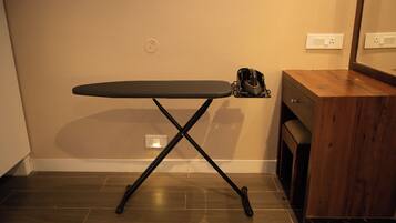 A compact ironing board with a stand, positioned against a wall with a wooden cabinet to the right.