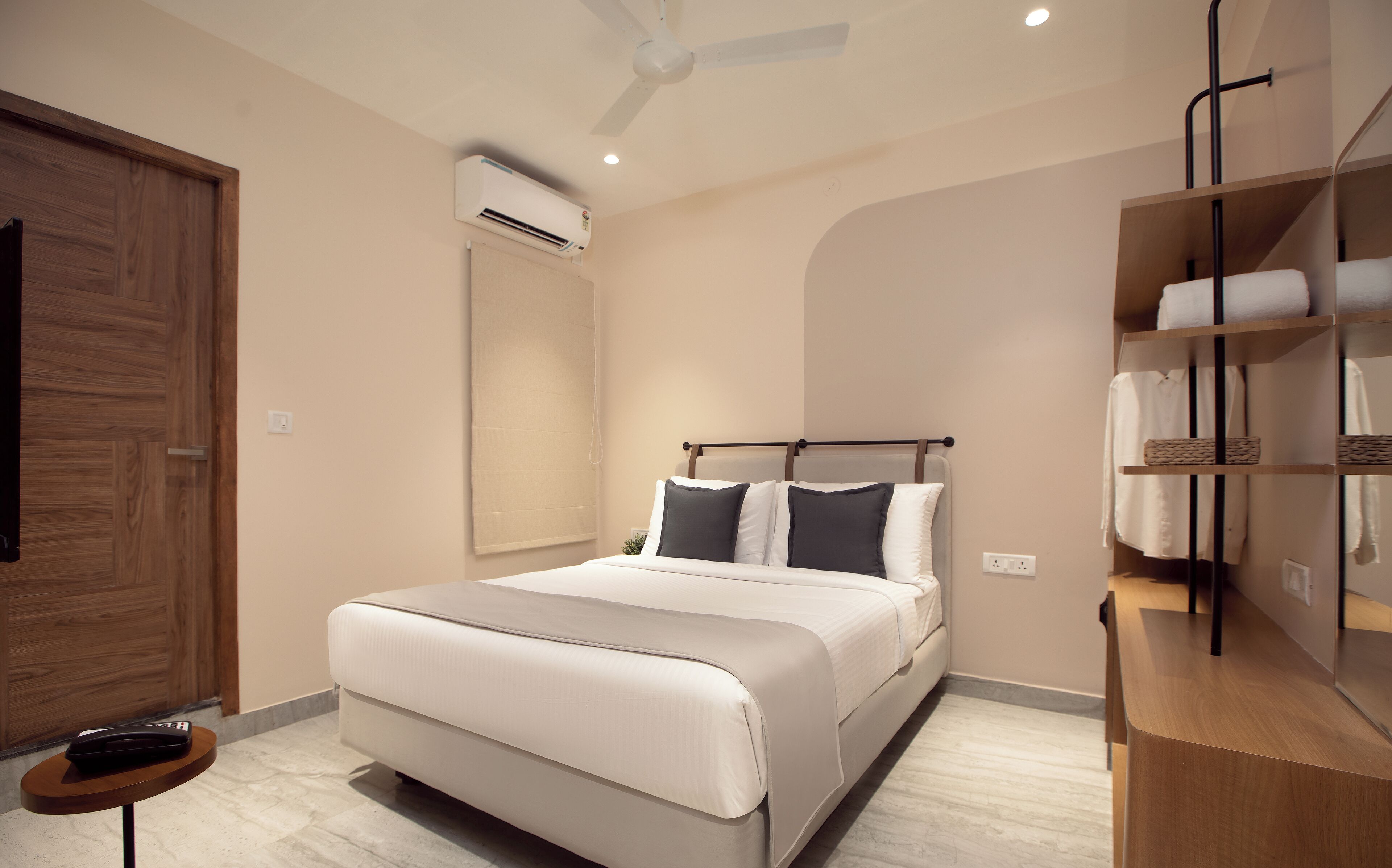 A modern bedroom with a large bed, a wooden wardrobe, an air conditioning unit, and a built-in shelf with towels.