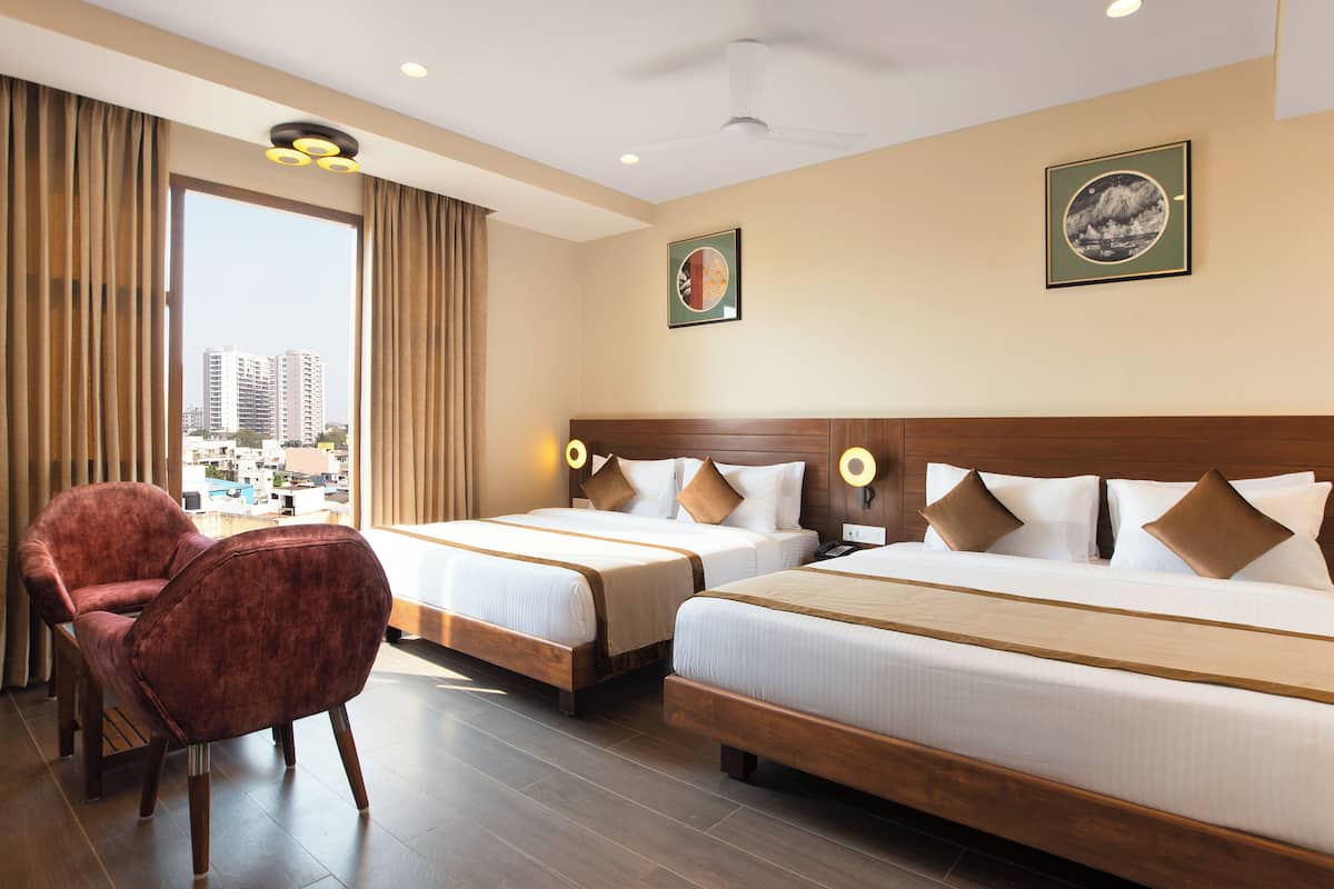 A hotel room with two beds, a red armchair, and a city view.