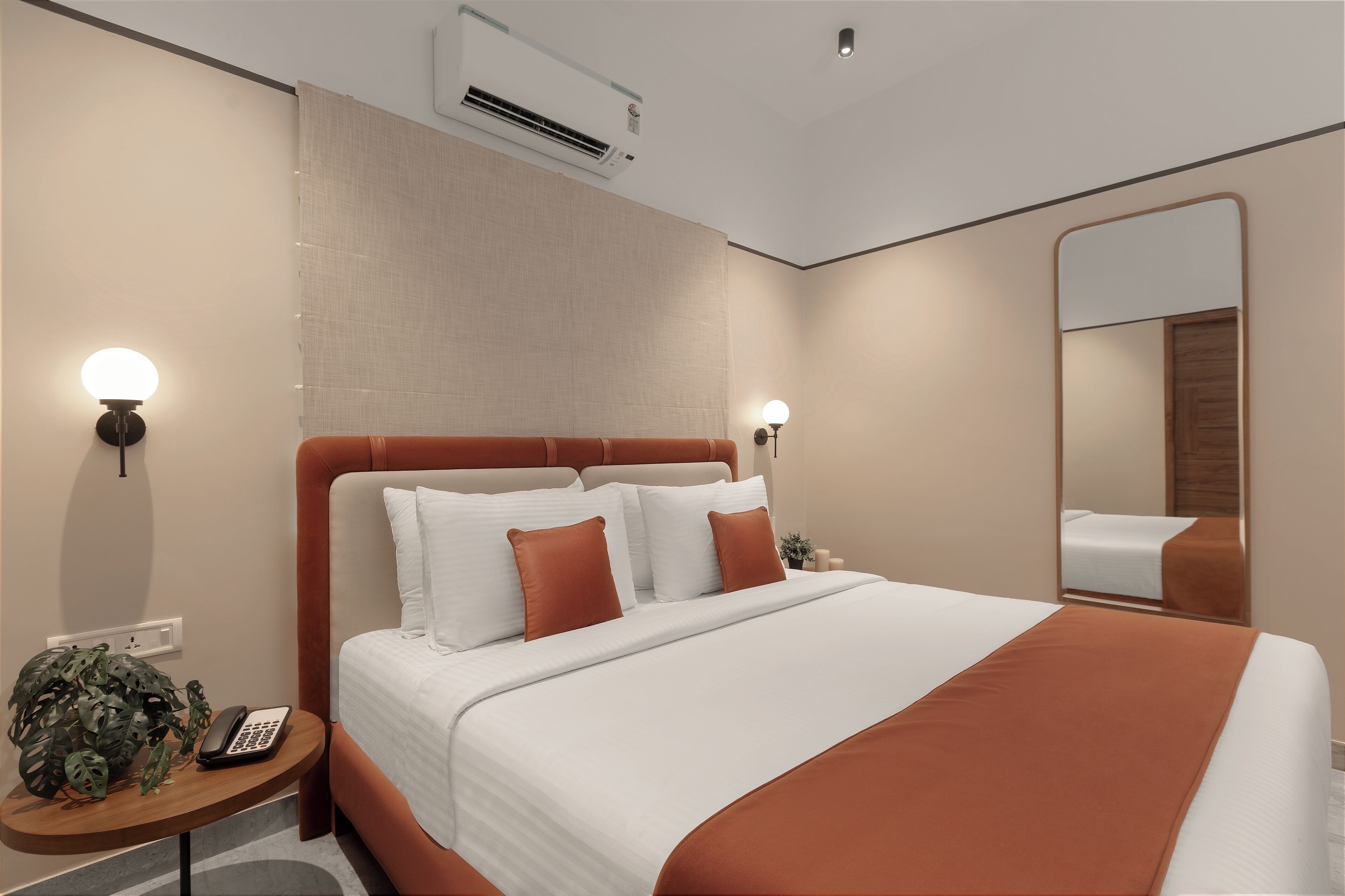 A hotel room with a large bed, two bedside tables, a mirror, and an air conditioning unit.