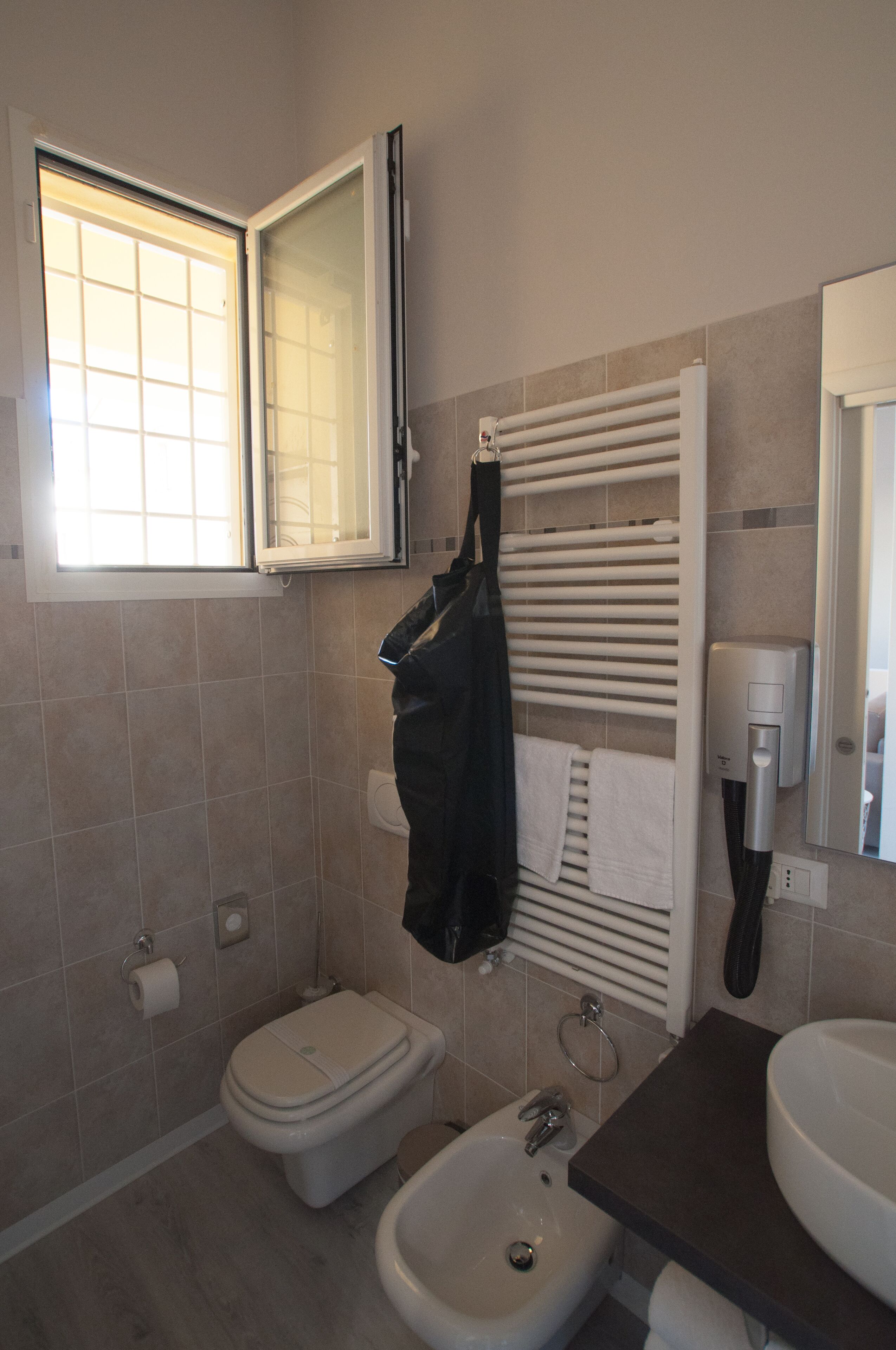 A bathroom with a toilet, bidet, towel rack, and a window.