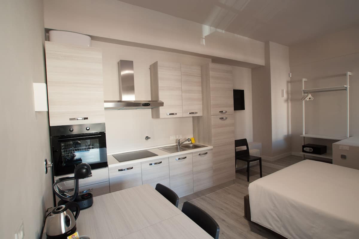 Eine moderne Küche mit eingebautem Ofen, einer Spüle und einem Herd. Ein Esstisch mit Stühlen und ein Bett mit weißer Bettdecke sind ebenfalls vorhanden.