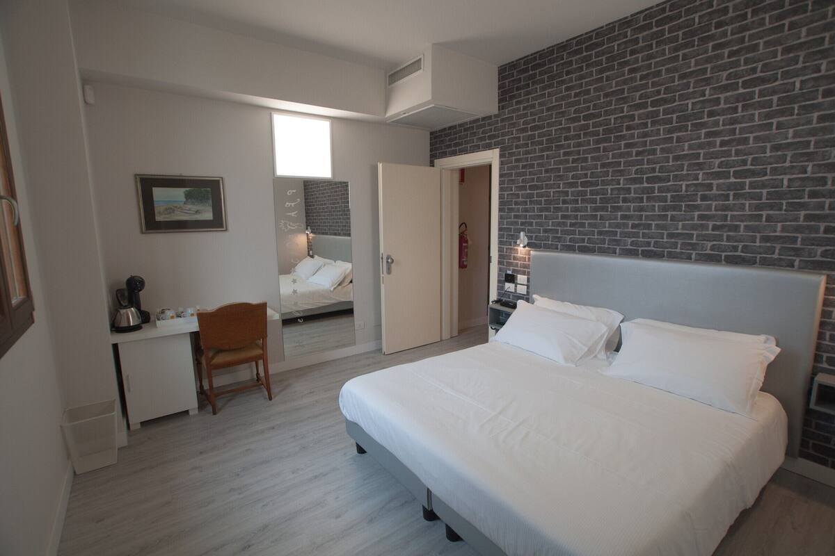 Ein Schlafzimmer mit Bett, Schreibtisch, Stuhl und einem durchgehenden Türrahmen sichtbarem Badezimmer.
