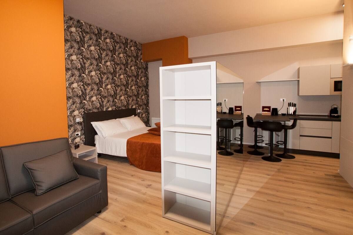 Ein modernes Hotelzimmer mit Bett, einer Couch, einem Essbereich mit Tisch und Stühlen sowie einer Küchenzeile.