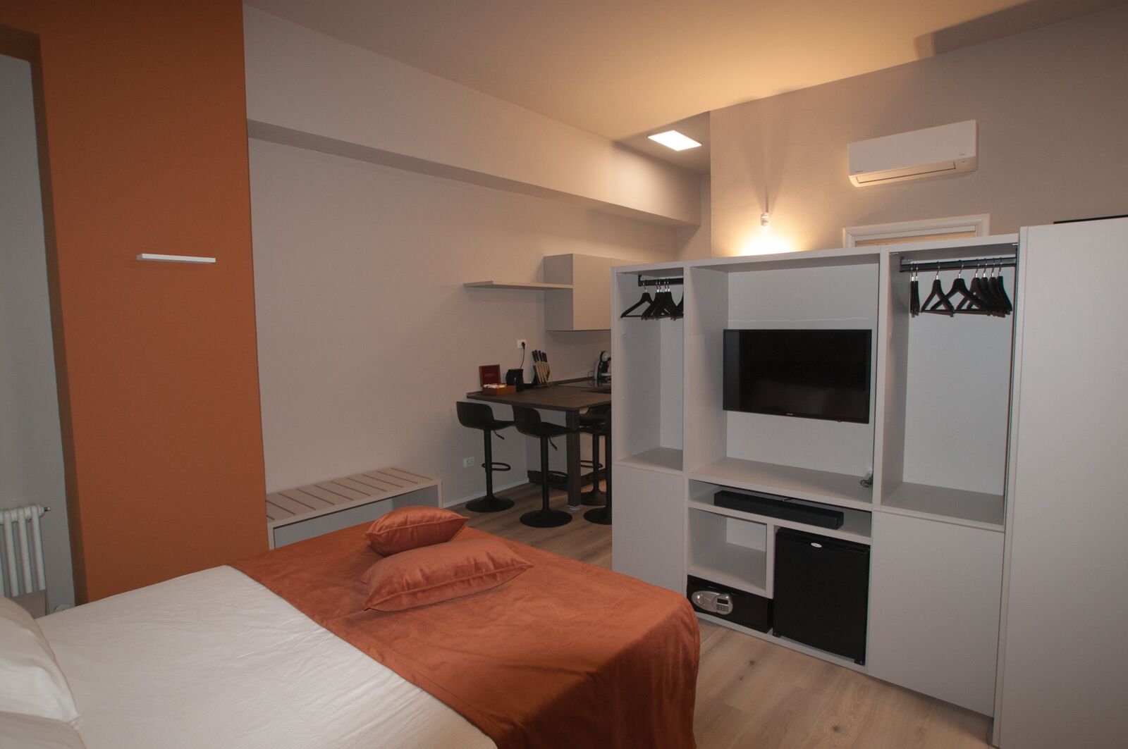 A modern hotel room with a bed, a desk with a chair, a TV, and a wardrobe.