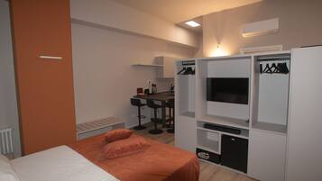 A modern hotel room with a bed, a desk with a chair, a TV, and a wardrobe.
