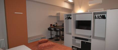 A modern hotel room with a bed, a desk with a chair, a TV, and a wardrobe.
