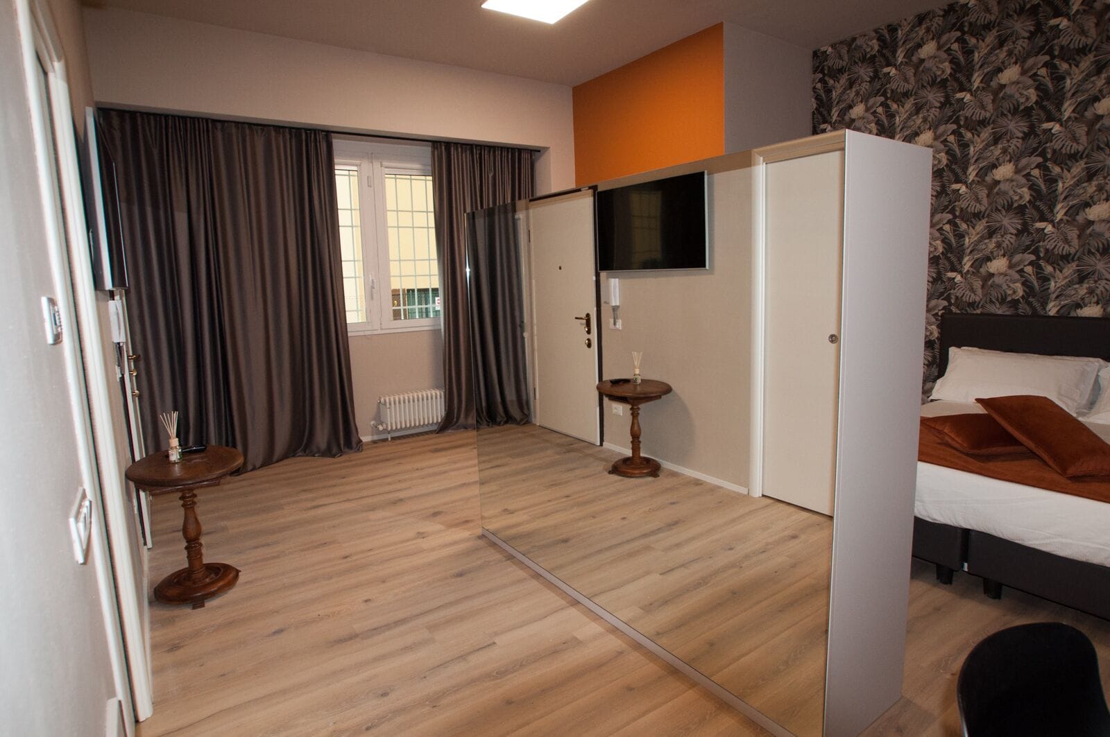 Una habitación de hotel con cama, televisor, radiador y ventana con cortinas.