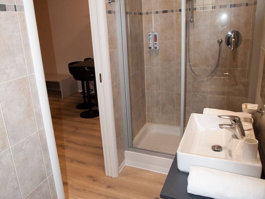 A modern bathroom with a glass-enclosed shower, a sink with a mirror, and a wooden floor.