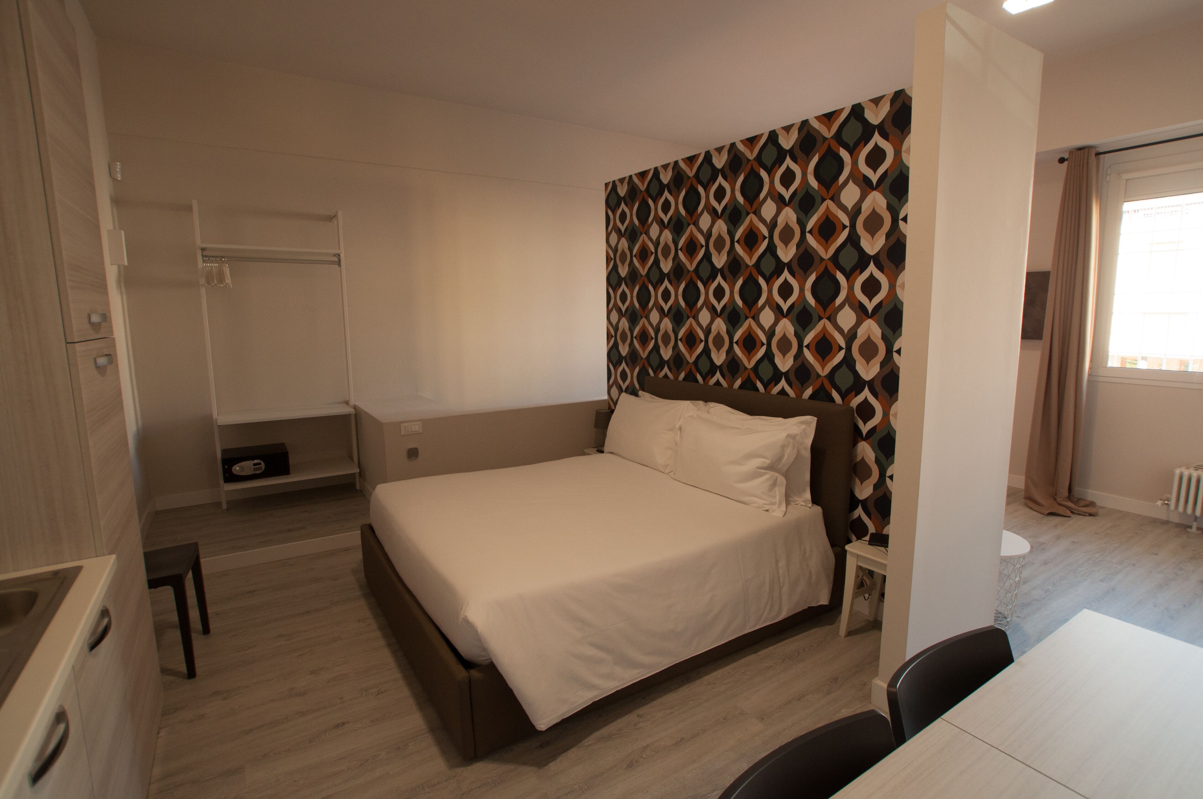 Ein Schlafzimmer mit einem Bett, einem Kleiderschrank, einem kleinen Tisch und einer Wand mit Muster.