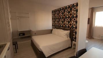 Un dormitorio con cama, armario, una mesita y pared decorada.
