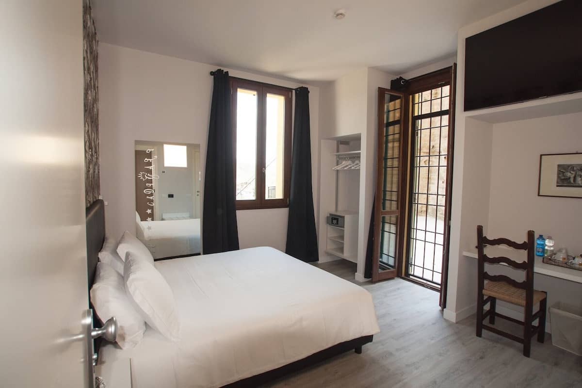 Ein Schlafzimmer mit Bett, Kleiderschrank, Schreibtisch mit Stuhl, Fenster mit Vorhängen und einer Tür.