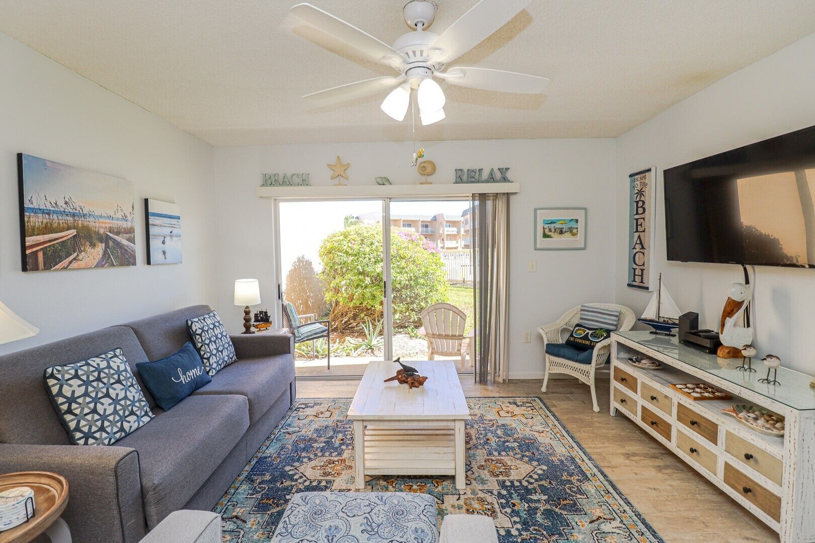 A living room with a grey sofa, patterned cushions, a coffee table, a TV, and a bookshelf.