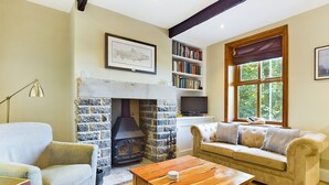 A cozy living room with a stone fireplace, a sofa, a coffee table, and a bookshelf. - Stoneswood Cottage, Delph, Saddleworth (Delph)