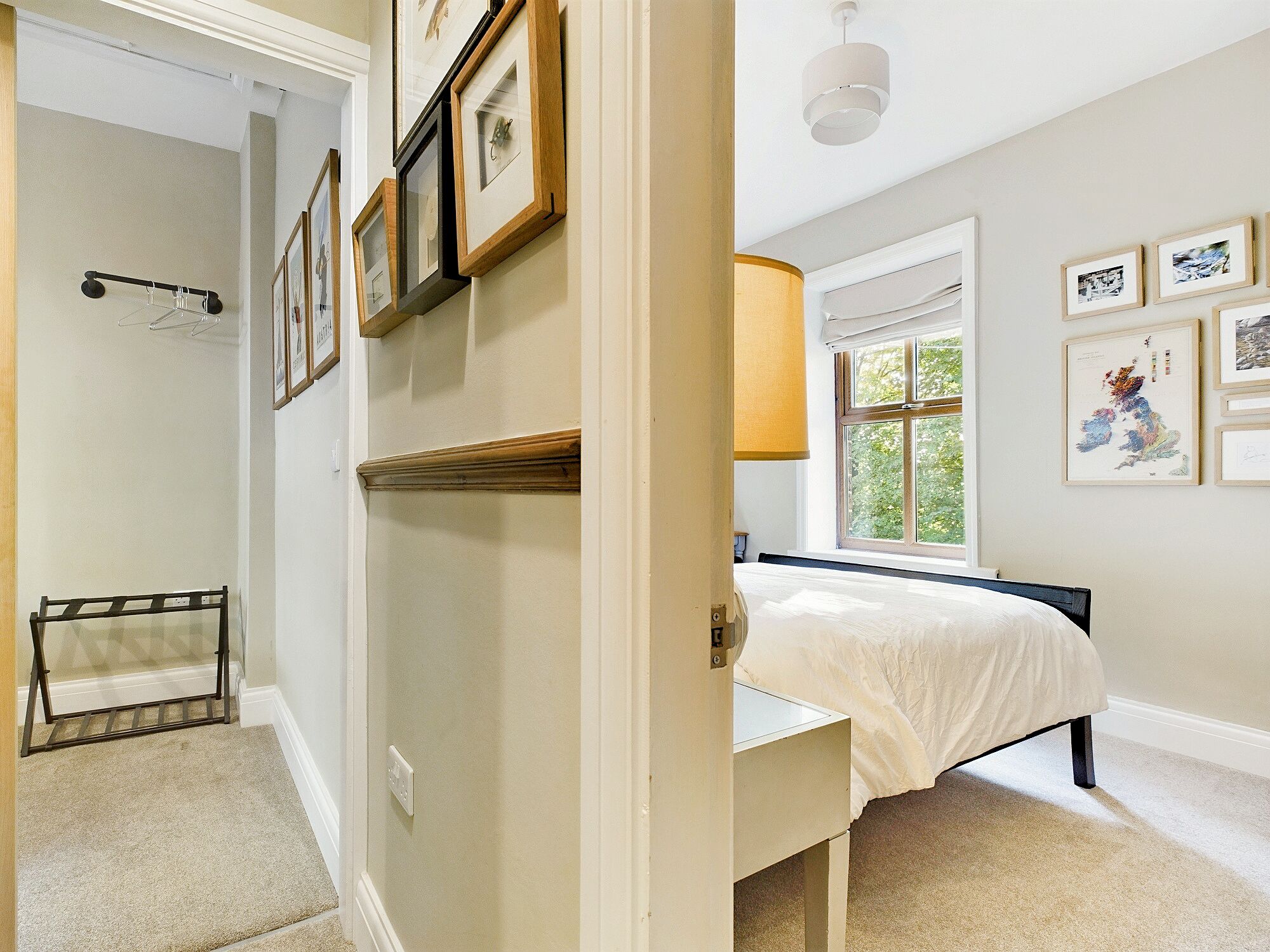 A bedroom with a bed, a window with a view, and a wall with framed pictures.