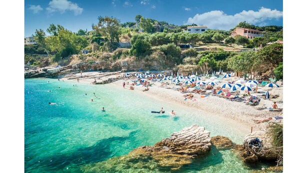 A beach with clear turquoise water, sun loungers, and umbrellas. - Close to the beach, spacious two-bedroom apartment with breakfast (Corfu)