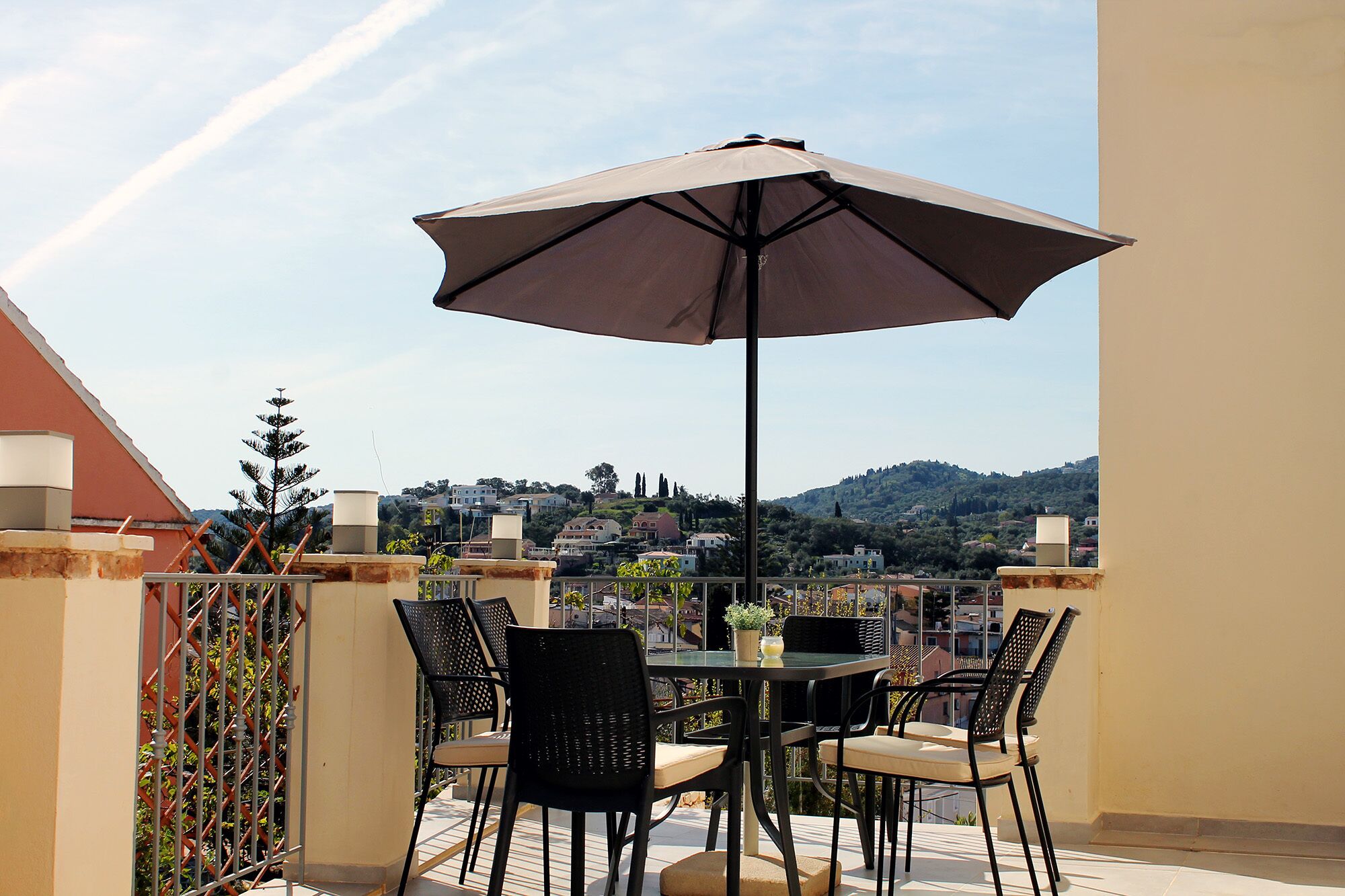 An outdoor patio with a table and chairs, a large umbrella, and a view of a hillside town.