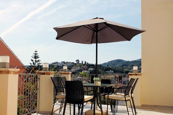 An outdoor patio with a table and chairs, a large umbrella, and a view of a hillside town.