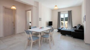 A modern living room with a dining area, a sofa, and a TV. - Close to the beach, spacious two-bedroom apartment with breakfast (Corfu)