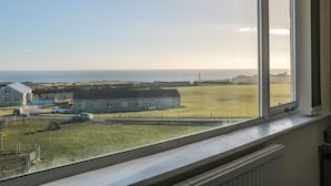 A view from a window overlooking a coastal landscape with a building, a grassy field, and the sea. - Lighthouse View (Portland)