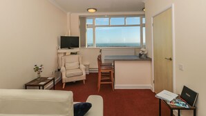 A compact living space with a kitchenette, a television mounted on the wall, a dining area, and a window with a view of the sea. - Lighthouse View (Portland)