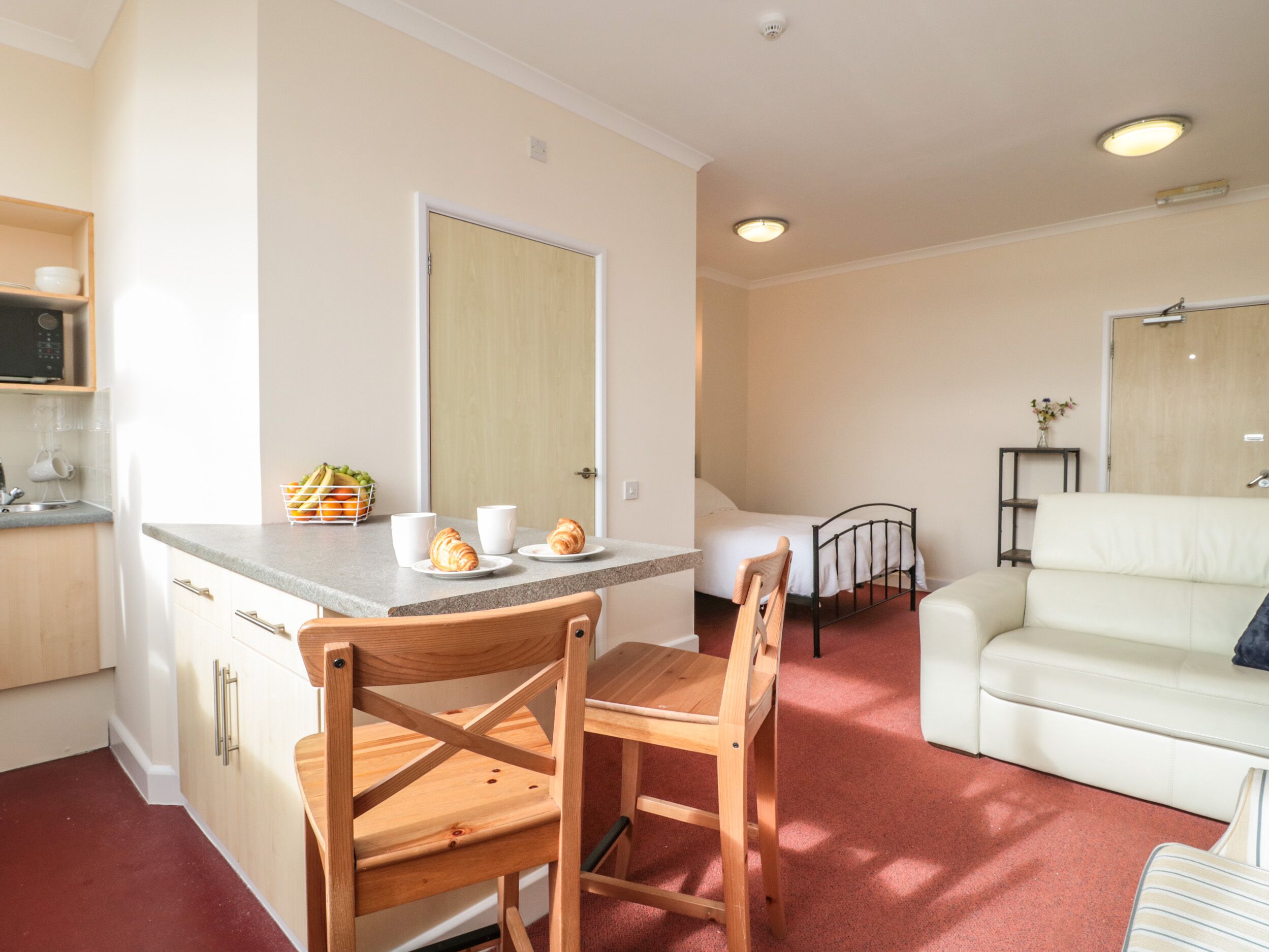 A compact living space with a kitchenette, a dining area with a wooden chair, a white sofa, and a small table with a vase.