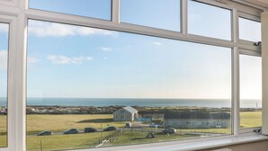 A view from a window overlooking a grassy field, a house, and the sea. - Lighthouse View (Portland)