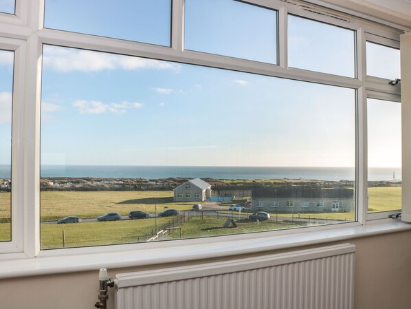 A view from a window overlooking a grassy field, a house, and the sea.