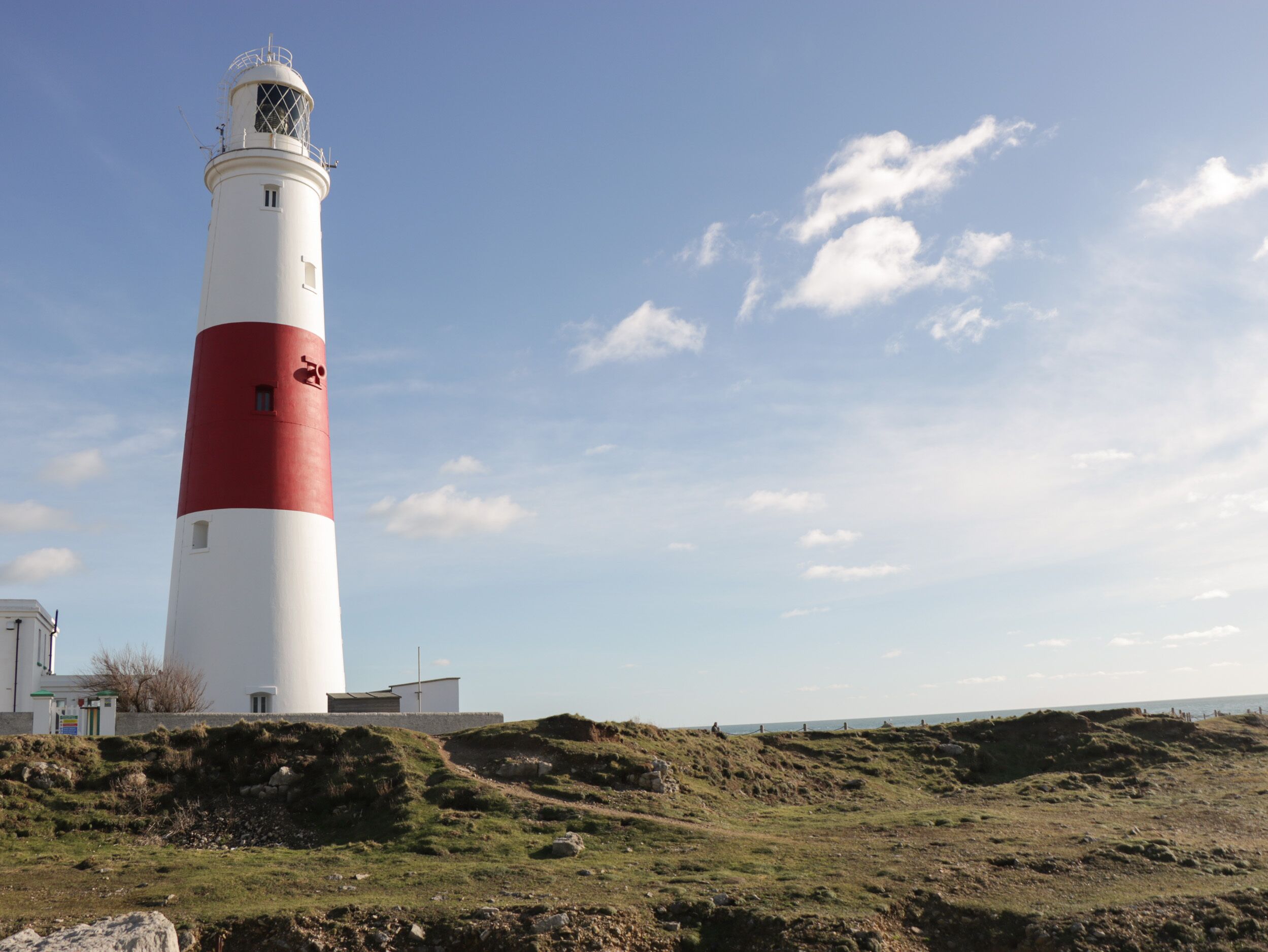 A lighthouse with a white and red exterior, situated on a grassy hill with a clear sky.