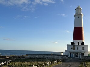 A lighthouse with a white and red exterior, a stone wall, and a building with a green roof in the foreground.