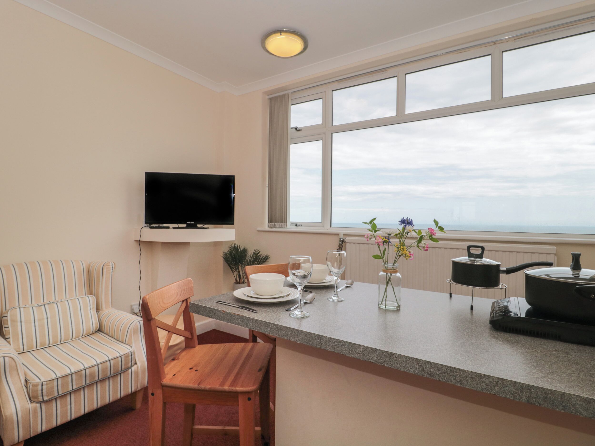 Una cocina moderna con un televisor de pantalla plana, un comedor con un sofá a rayas y un amplio ventanal con vistas al cielo.