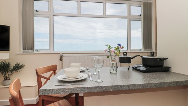 A kitchen with a dining table, chairs, a window with curtains, a potted plant, and a pot on the counter. - Lighthouse View (Portland)