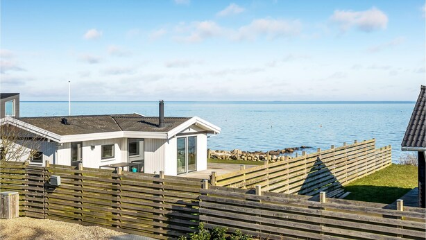 En fastighet vid kusten med ett trädäck, en vit byggnad med stora fönster och utsikt över havet.