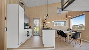 Ett modernt kök med vita skåp, en köksö och en matplats med svarta stolar och ett träbord.