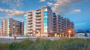 Ein mehrstöckiges Hotel mit Balkonen in Strandnähe, vor dem ein Rasen und ein Zaun zu sehen sind.