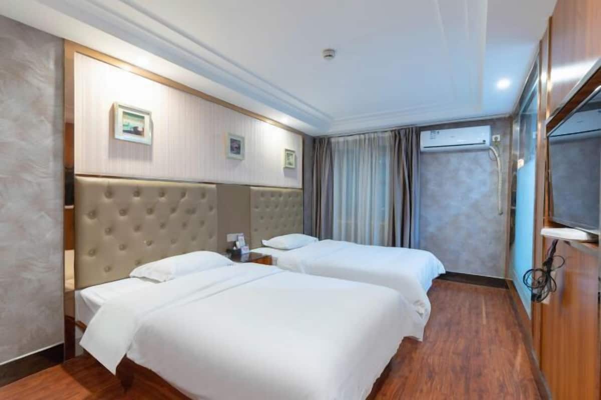 Une chambre d’hôtel avec deux lits, une grande tête de lit rembourrée, un téléviseur à écran plat et un appareil de climatisation.