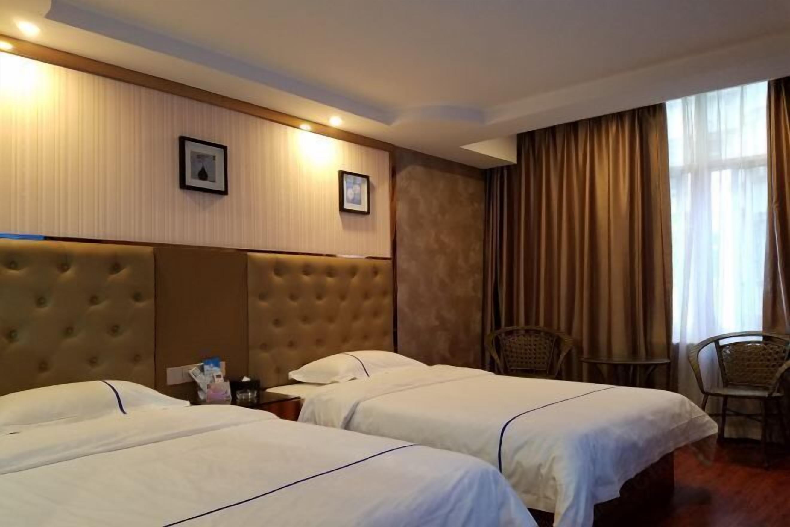 A hotel room with two beds, a headboard, a small table, and a chair.
