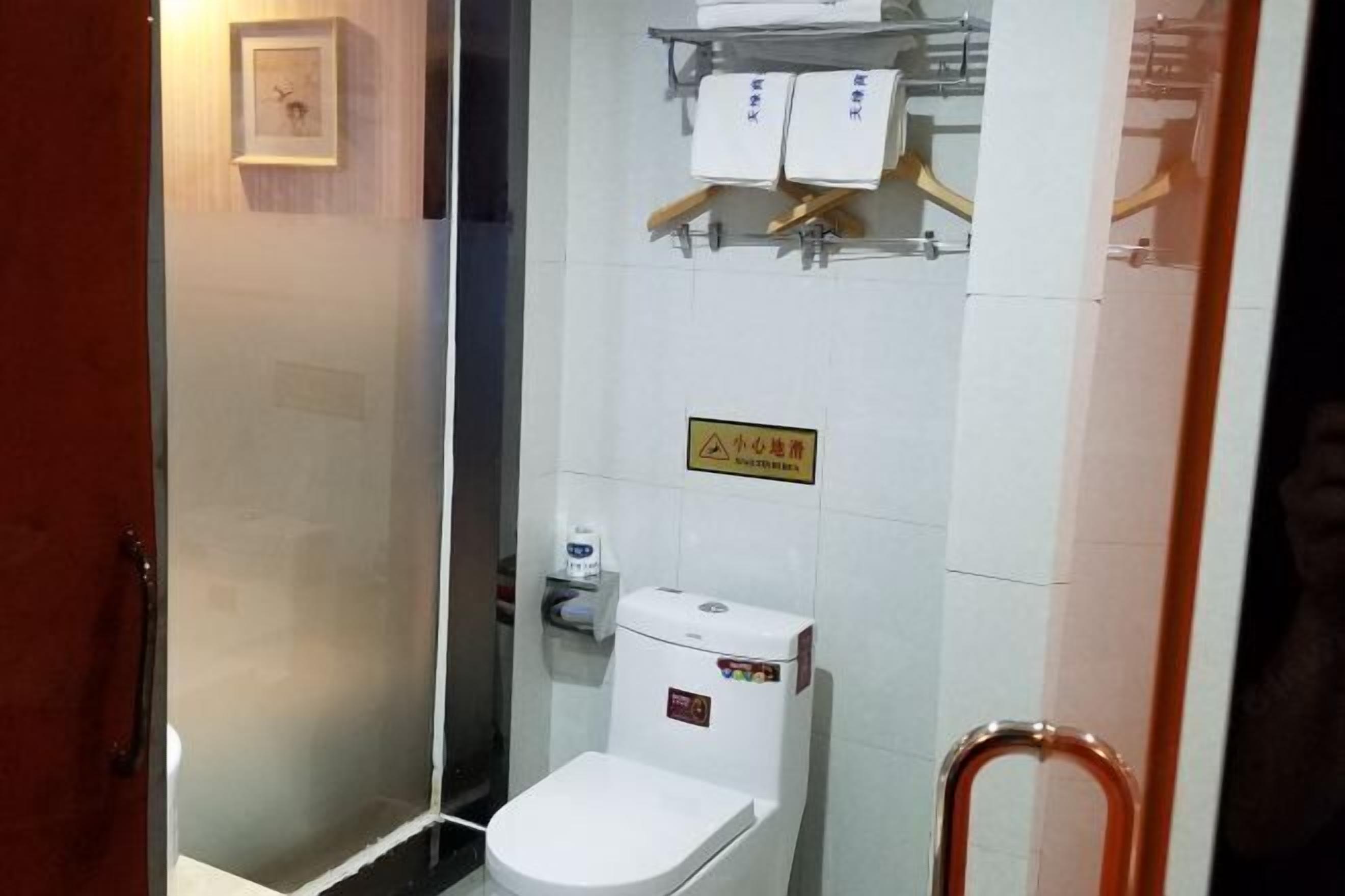 A bathroom with a toilet, a glass partition, a towel rack with towels, and a sign on the wall.