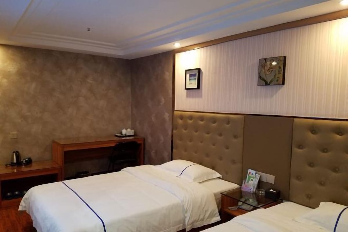 A hotel room with two beds, a wooden desk, a nightstand, and a wall-mounted TV.