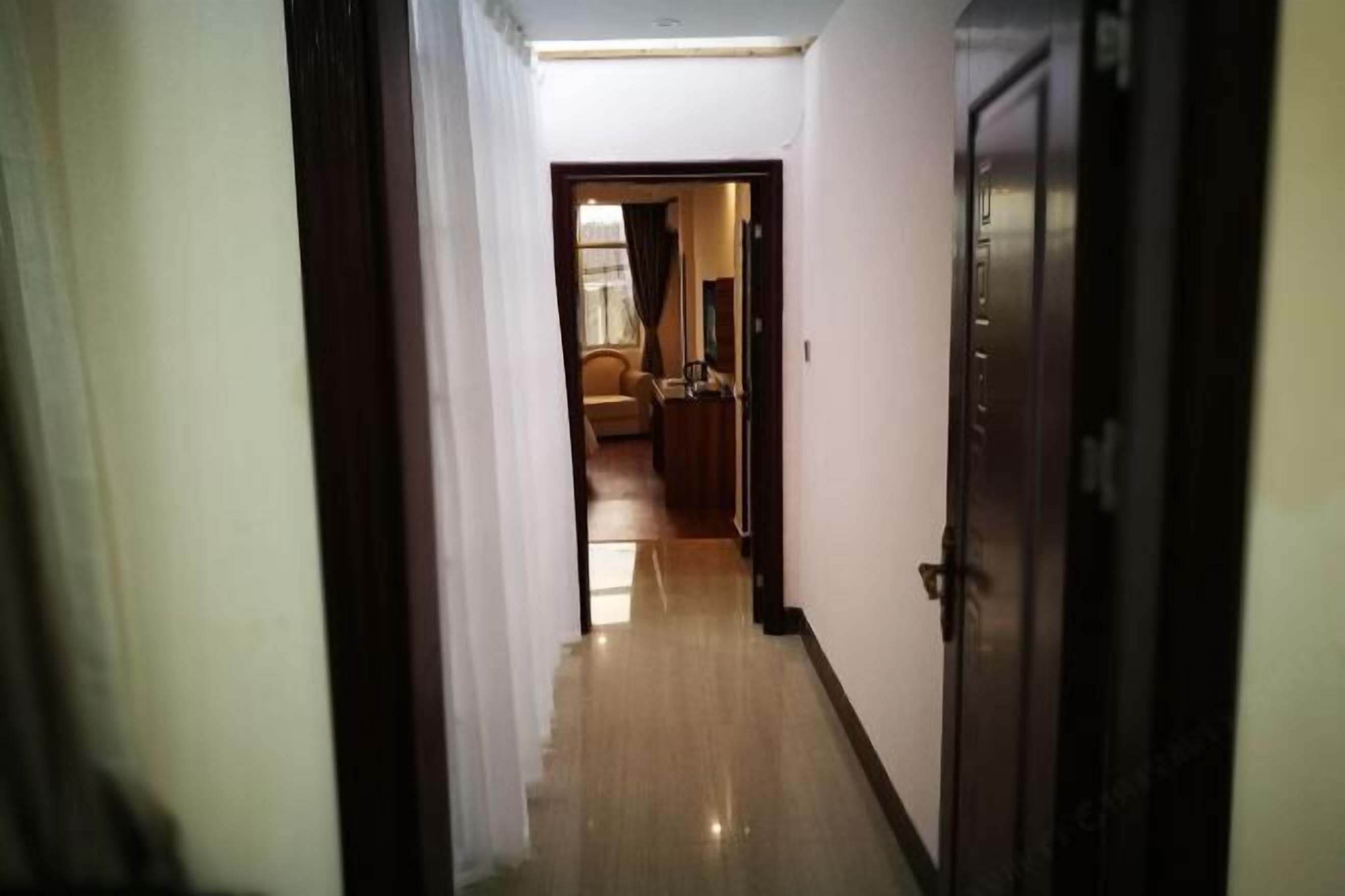Corredor que leva a um quarto com piso de madeira e uma porta à direita.