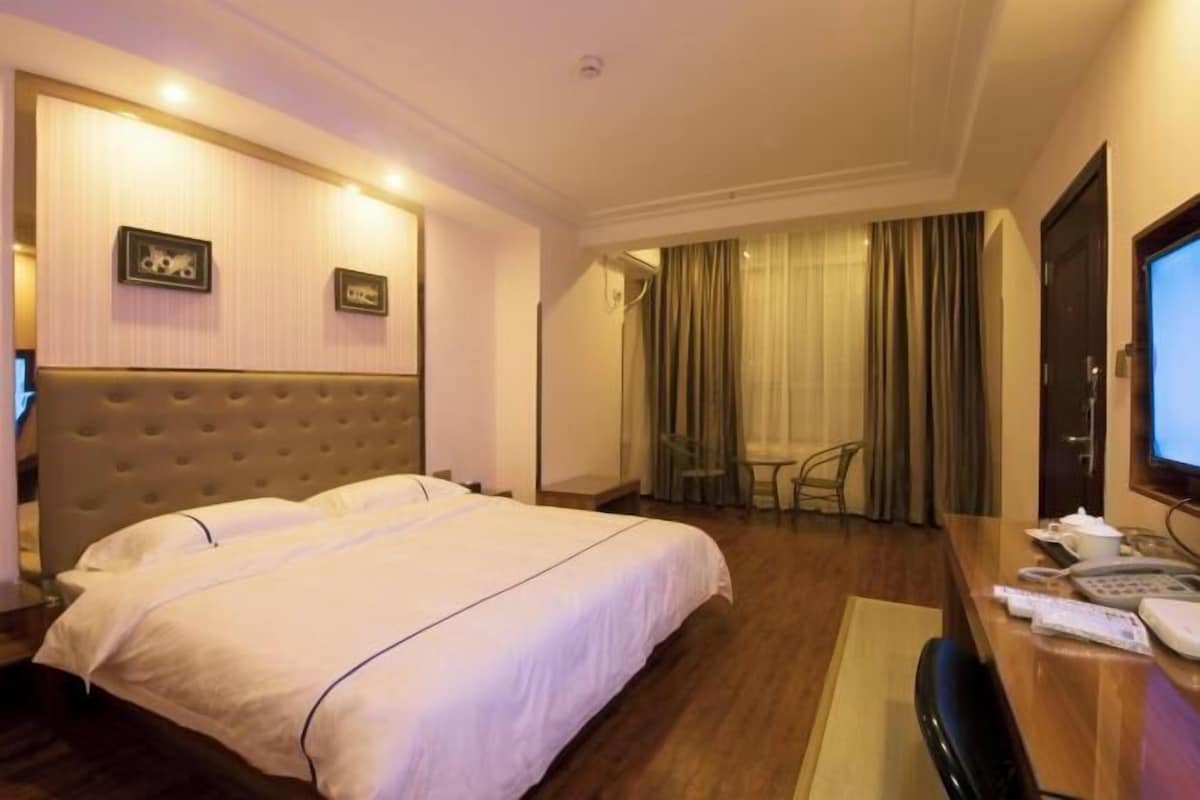 A hotel room with a large bed, a desk with a telephone, and a television.