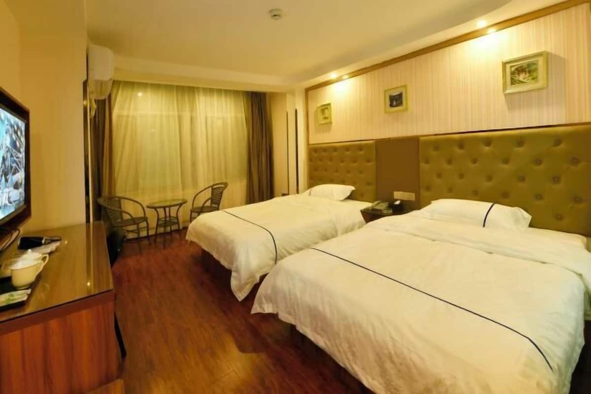 Une chambre d’hôtel avec deux lits, une télévision, un bureau avec une chaise et une fenêtre avec des rideaux.